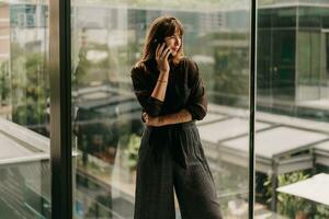 Stylish business woman in fashionable casual outfit  talking by mobyle phone  during work day in  modern business center. photo