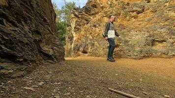 A male traveler with a backpack walks past large brown rocks in the mountains of Poland video