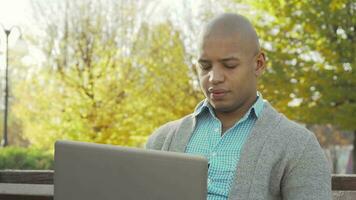 African American man working on laptop at local park in autumn video