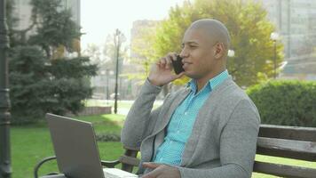 Handsome African American businessman using smart phone and laptop outdoors video