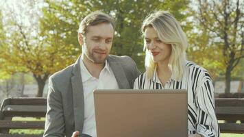 Two business colleagues using laptop at the park together video