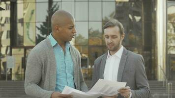 Two businessmen examining documents in front of business building video