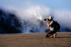 a man taking a photo of a wave crashing on the beach