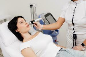 Woman undergoing a cosmetic procedure in a beauty salon. A woman undergoes fractional RF lifting against a light background. Advertising concept for clean and young facial skin. photo