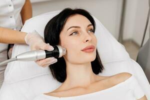 Woman undergoing a cosmetic procedure in a beauty salon. A woman undergoes fractional RF lifting against a light background. Advertising concept for clean and young facial skin. photo