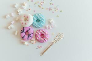 Top view of Marshmallows and Colorful donuts with a golden whisk on white table photo