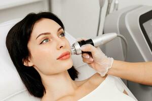 Woman undergoing a cosmetic procedure in a beauty salon. A woman undergoes fractional RF lifting against a light background. Advertising concept for clean and young facial skin. photo