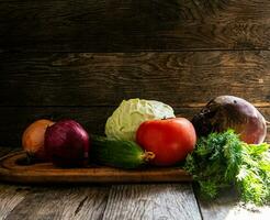 Onions, cabbage, tomatoes, cucumbers, beets, parsley and herbs lie on a cutting board in the kitchen, on a wooden table. photo