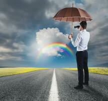 Businessman cover himself with an umbrella and watches far with a binocular photo