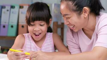 Mother and daughter drawing together with crayons. Adult woman helps girl study or draw together at home in living room. Happy family. video