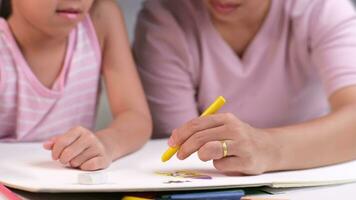 madre y hija dibujo juntos con lápices de color. adulto mujer ayuda niña estudiar o dibujar juntos a hogar en vivo habitación. contento familia. video