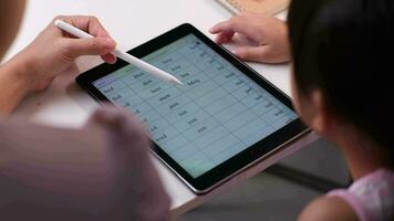 Lycklig liten asiatisk dotter talande med mor använder sig av digital läsplatta till do läxa eller studie uppkopplad. Lycklig ung flicka och vuxen Sammanträde på tabell inlärning på ipad tillsammans. tillbaka till skola. video