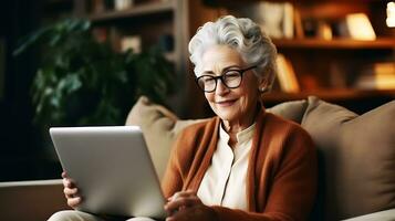 A beautiful pensioner woman looks into a laptop and smiles. A woman is sitting at home, studying something, chatting online or watching a video. AI Generative photo