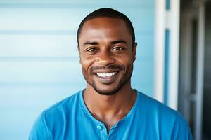 A young African-American man in a blue t-shirt stands in front of a blue wall, looks at the camera and smiles. AI Generative photo