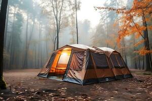 A large tourist tent stands in the middle of the forest in foggy rainy autumn weather. The lantern is on in the tent. AI Generative photo