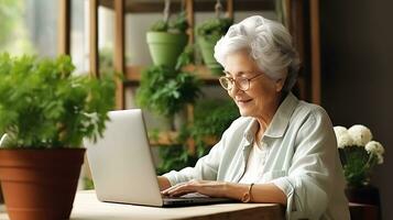 A beautiful pensioner woman looks into a laptop and smiles. A woman is sitting at home, studying something, chatting online or watching a video. AI Generative photo
