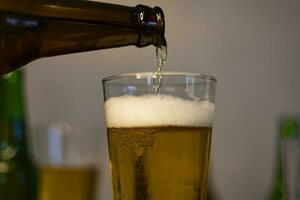 Close-Up. Pouring Beer In Glass. Beer is poured from dark brown bottle into beer glass. photo