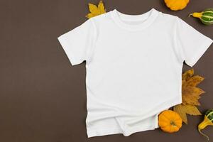 White man or women cotton t-shirt mockup with pumpkins and fallen leaves on dark background. Design t shirt template, print presentation mock up. Top view flat lay. photo
