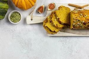 Pumpkin bread, cake on a wooden cutting board with pecan nuts, pumpkin seeds and cinnamon spices on a light gray background with colorful pumpkins and figs. Top view. Copy space. photo