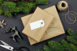 Christmas handmade gift box with label tag mockup, pine cones, fir tree branches and decoration on dark background. Festive styled composition. Top view. photo