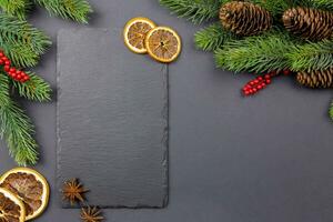 Winter dried fruits and culinary spice background mockup with christmas tree branches and pine cones on dark background with a black slate chalkboard for your text. Top view. Copy space. photo