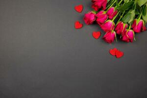 Red roses flowers and hearts confetti on dark background. Valentines, mothers, womens day, wedding or birthday flat lay concept. Top view. Copy space. photo