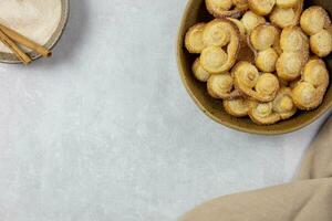 Puff pastry eyelet, Palmier cookies in a bowl with cinnamon and sugar on the light concrete background. Top view. Copy space. photo