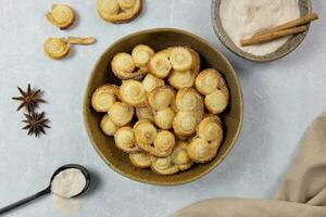 Puff pastry eyelet, Palmier cookies in a bowl with cinnamon and sugar on the light concrete background. Top view. photo