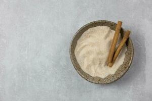 Cinnamon sugar with cinnamon sticks in a bowl on light concrete background. Top view. Copy space. photo