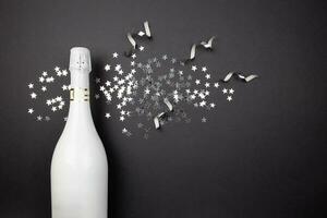 Champagne bottle and confetti on dark background. Flat lay composition of celebration. Top view. Copy space. photo