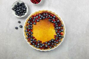 Delicious cheesecake tart with fresh blueberries and cranberries on a light gray concrete background. Top view. photo
