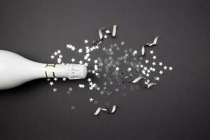 Champagne bottle and confetti on dark background. Flat lay composition of celebration. Top view. photo