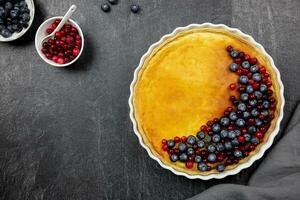 Delicious cheesecake tart with fresh blueberries and cranberries on a dark stone background. Top view. Copy space. photo