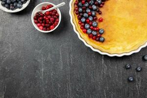 Delicious cheesecake tart with fresh blueberries and cranberries on a dark stone background. Top view. Copy space. photo