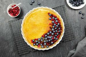 Delicious cheesecake tart with fresh blueberries and cranberries on a dark stone background. Top view. photo