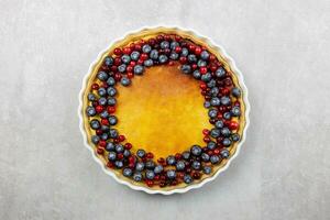 Delicious cheesecake tart with fresh blueberries and cranberries on a light gray concrete background. Top view. photo