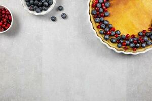 Delicious cheesecake tart with fresh blueberries and cranberries on a light gray concrete background. Top view. Copy space. photo