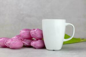 Classic white mug mockup with pink tulips flowers on light gray concrete background. Valentines, mothers, womens, 8 march or birthday concept. Side view. Copy space. photo