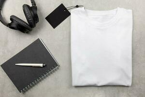White womens cotton Tshirt mockup with spiral notebook and black headphones. Design t shirt template, print presentation mock up. Top view flat lay. Concrete stone background. photo