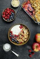 Bowl of homemade granola with yogurt and fresh berries on dark stone concrete background. Cranberry and apple crumble, crisp with almond flakes and oat. Top view. photo