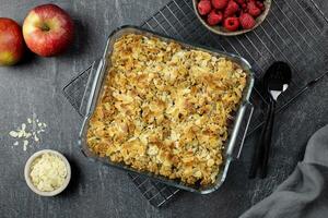 Cranberry and apple crumble, crisp in a glass baking dish with almond flakes and fresh berries on dark stone concrete background. Top view. photo