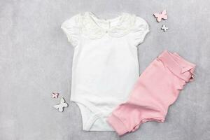 White baby girl bodysuit mockup flat lay with pink panties on the gray concrete background. Design onesie template, print presentation mock up. Top view. photo