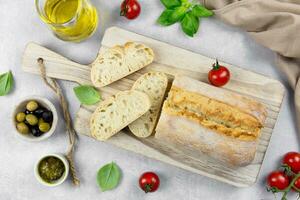 Fresh italian ciabatta bread with herbs, olive oil, black and green olives, basil leaves and pesto sauce on light gray concrete background. Top view. photo
