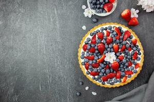 Delicious blueberry and strawberry tart with whipped cream and mascarpone on a dark stone background. Top view. Copy space. photo