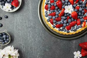 Delicious blueberry and strawberry tart with whipped cream and mascarpone on a dark stone background. Top view. Copy space. photo