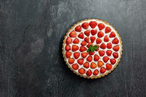 Delicious strawberry tart with whipped cream and mascarpone on a dark concrete background. Top view. Copy space. photo