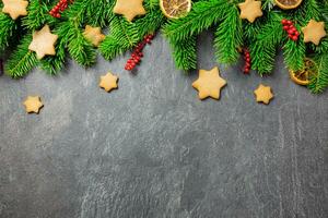 Christmas traditional gingerbread stars with decoration, spices and christmas tree branches on a dark stone background. Top view. Copy space. photo