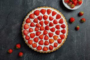 Delicious strawberry tart with whipped cream and mascarpone on a dark concrete background. Top view. photo