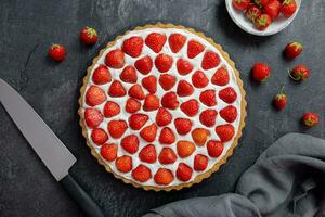 Delicious strawberry tart with whipped cream and mascarpone on a dark concrete background. Top view. photo