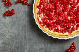 Redcurrant cheesecake, tart with fresh berries in a white baking dish on dark gray background. Top view. Copy space. photo
